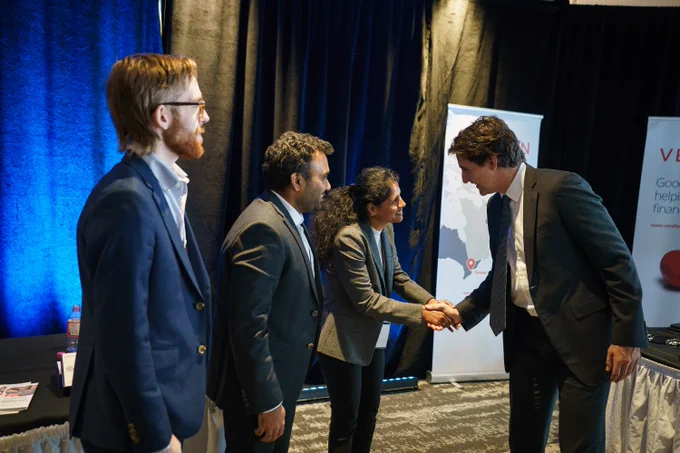 Prime Minister Justin Trudeau is standing and shaking hands with a woman, who is standing in front of him. Both of them are smiling. Two men are standing beside the woman. 