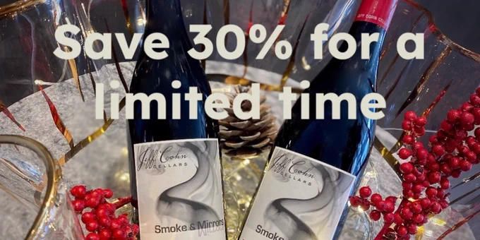 Two bottles of Jeff Cohn Cellars Smoke & Mirrors in a festive bowl with twinkle lights, pine cones and red berry twigs.