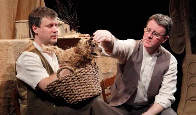 Two men and a puppet animal on stage.
