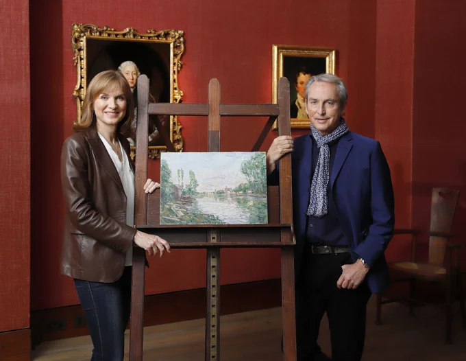 Fiona Bruce and Philip Mould stand next to a painting on an easel.