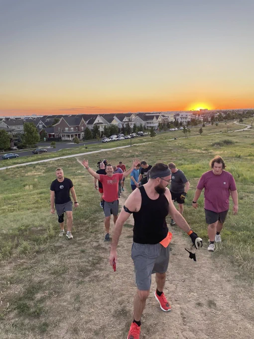 Men walking backwards down a hill with sunrise in the background.