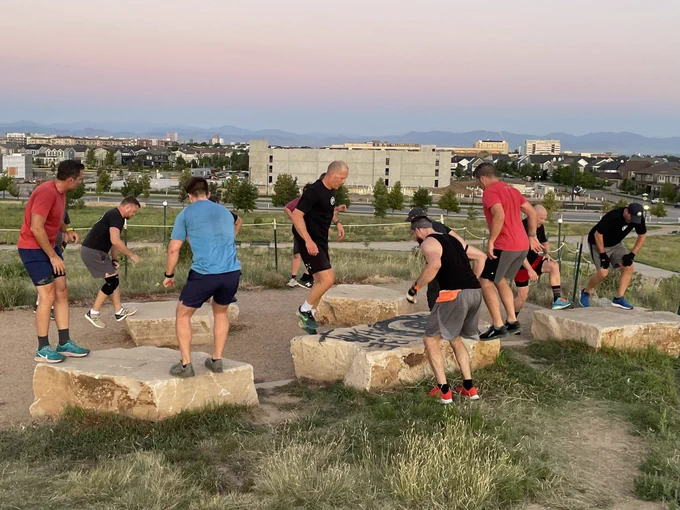 Group of men doing box jumps on low flat boulders.