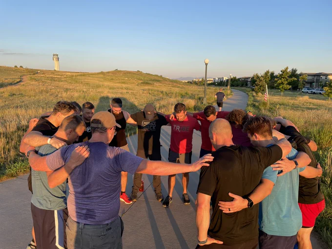 Circle of trust (prayer). Men with arms on shoulders in a circle, heads bowed.