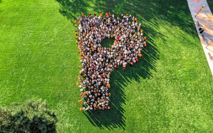 Hundreds of incoming students arranged to create the letter P on a field of green grass. 