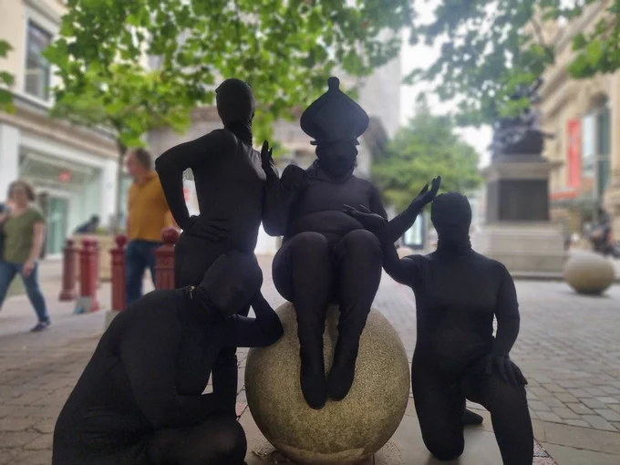 Four performers dressed in black morph suits representing chess pieces are beautifully arranged around (and on top of) an outdoor stone bolder