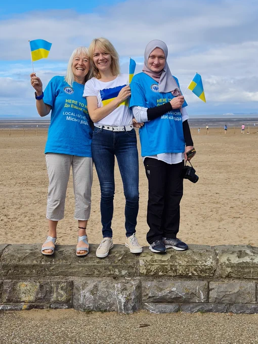 Members of the Migration Team smiling and waving Ukrainian flags on Weston-Super-Mare beach.