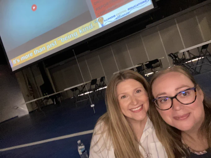 Close up of Lindsay and Stefanie with the bottom of the presentation screen behind them. The bottom of the slide reads, “It’s more than just ‘being kind’#.’” The Illinois Digital Educators Alliance logo is visible in the bottom right corner.