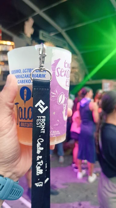 Vaso reutilizable de fiestas con un lanyard del FrontFest. De fondo una txosna de la Aste Nagusia de Bilbao. 