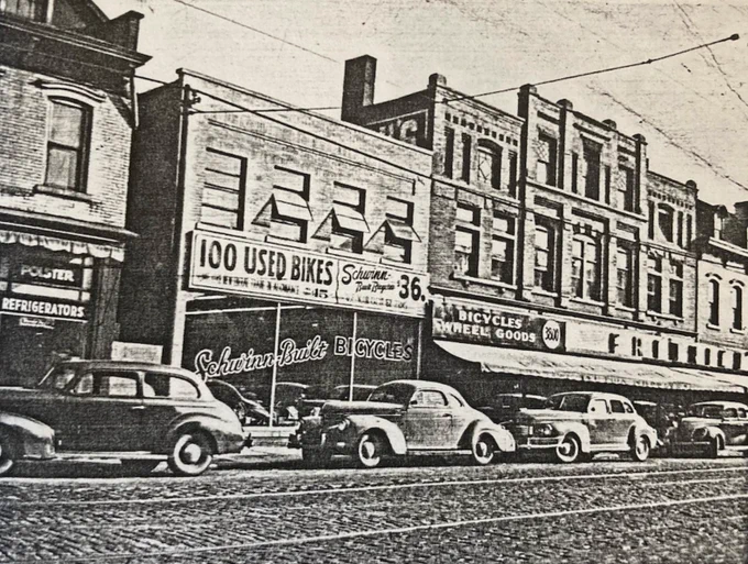 Early 1940s photo showing old cars parked on Lorain Avenue in front of the storefronts housing Fridrich Bicycle. Signs read "100 Used Bikes," "Schwinn Built Bicycles $36," and "Bicycles | Wheel Goods | FRIDRICH." Photo courtesy of Nancy Todd Paris, descendant of Joseph Fridrich