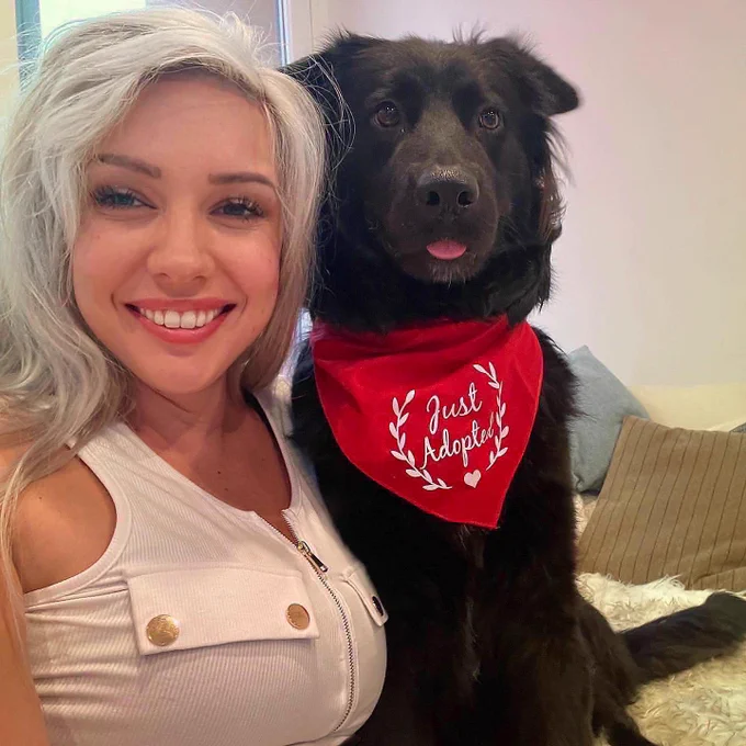 A picture of me next to a black dog. He is wearing a bandana that says “just adopted”