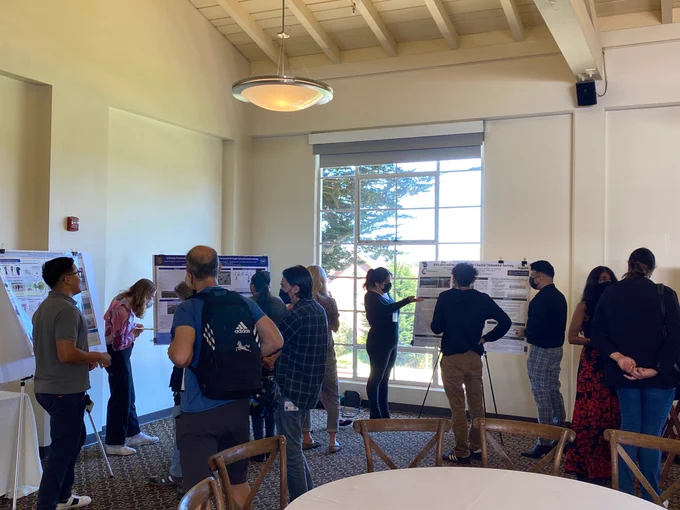 Students and professors at scientific posters in a conference room, sharing research projects on seaweed and genomics, education, and other topics
