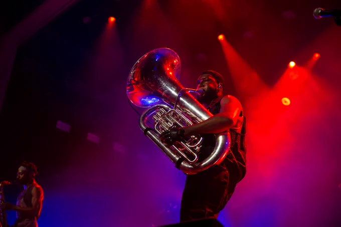 A man plays a tuba, with purple and red haze lit
behind him.