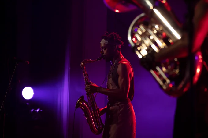 A man in side profile plays a saxophone, with a tuba
blurry in the foreground.