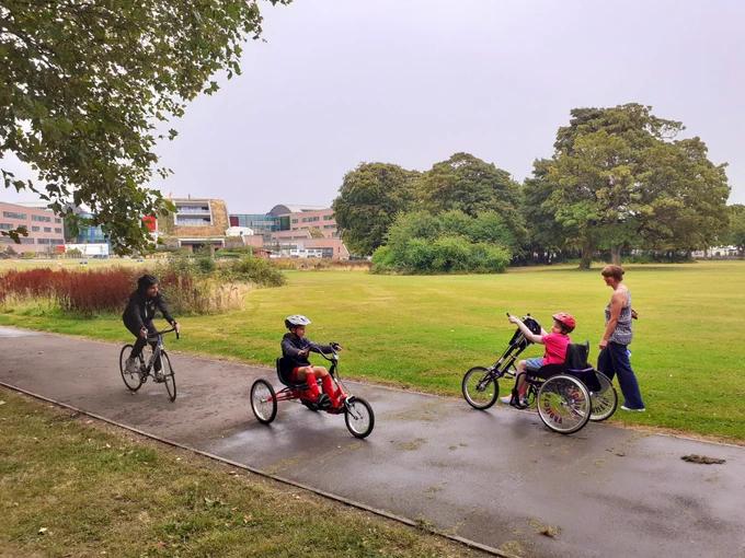 Two young cyclists using a handcycle and semi-recumbent trike in Springfield Park, Liverpool, close to Alder Hey Children's Hospital 