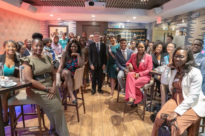 Secretary Blinken poses for a phot with around 25 young people inside a restaurant.