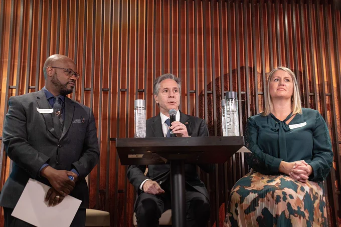 Secretary Blinken, Senior Official for Public Diplomacy and Public Affairs Liz Allen, and another man sit at a tall table. Secretary Blinken speaks into a microphone.