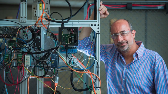 George Lordos is leaning on a piece of equipment with cables and wires going in every direction.