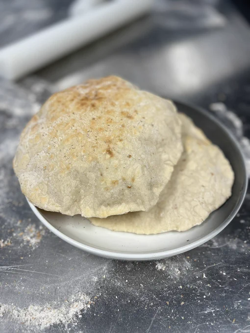 Two pieces of flat bread in a bowl on an industrial table covered with flour