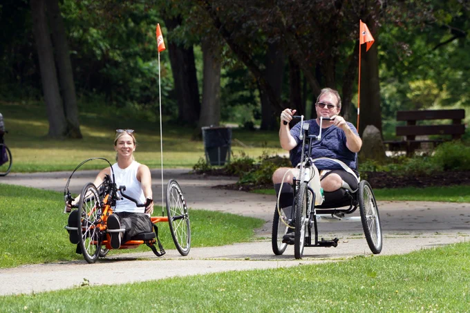 Two people ride adapted bikes along a trail