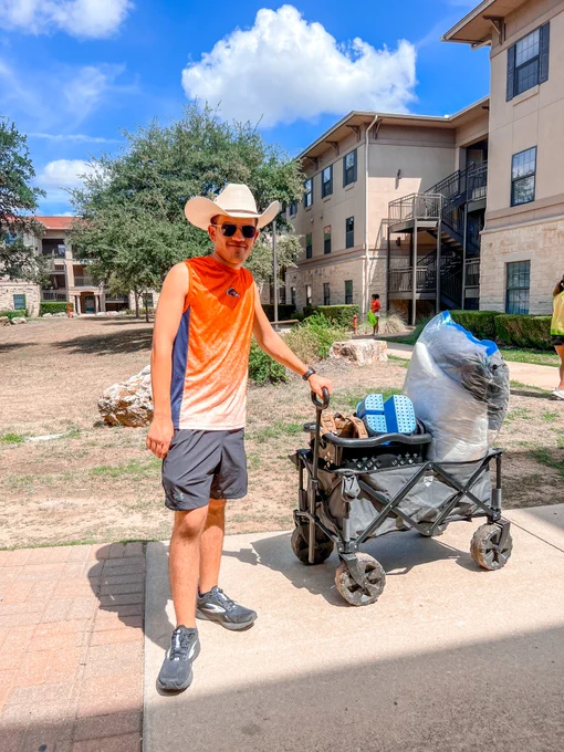 A resident is moving in. They are smiling at the camera while holding their move in cart by the handle. 