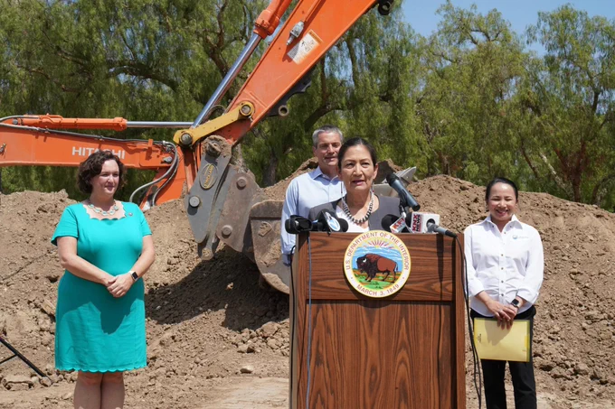 Woman speaks at podium with two women, a man and machinery in the background