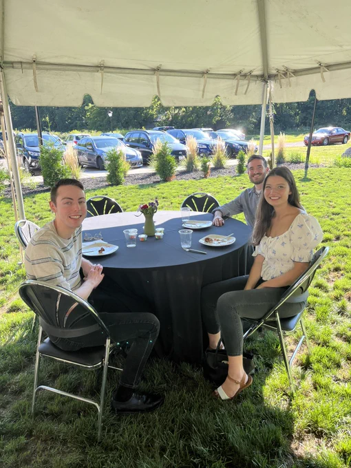 Chris, Destiny, and Corey sit around a table under a tent outside