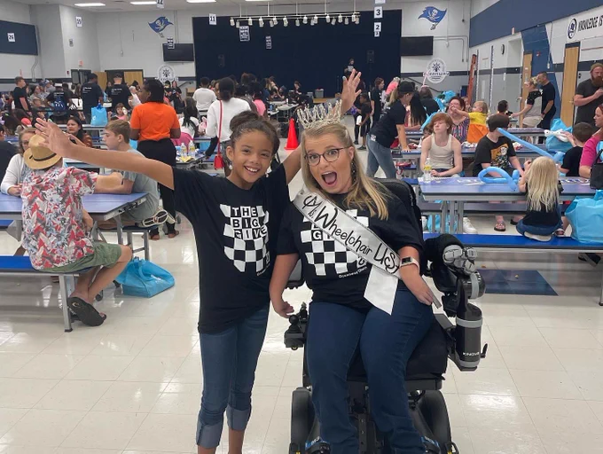 Open mouth pose in the big give shirt with crown and sash on in front of a crowd.