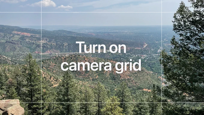 How to turn on camera grid. A landscape photo with pine trees in the foreground, a hill with a highway wrapping around it in the middle distance, and flat terrain extending to the horizon in the far distance. A semi-transparent white grid is overlaid on the photo, dividing it into nine sections.
