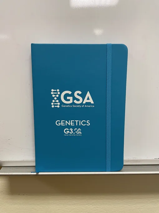 A small blue notebook with the GSA, GENETICS, and G3 logos on the cover in white.
