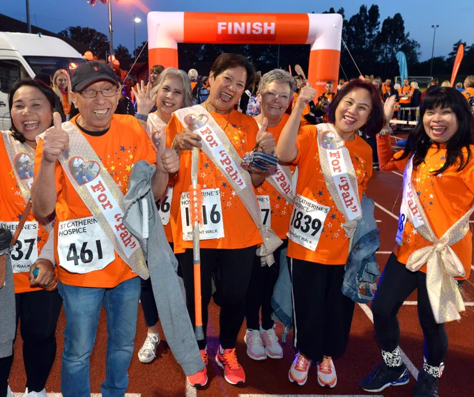 Group of Midnight Walkers in orange t-shirts and sashes that read 'for "Pah", laughing, smiling and cheering at the camera. 