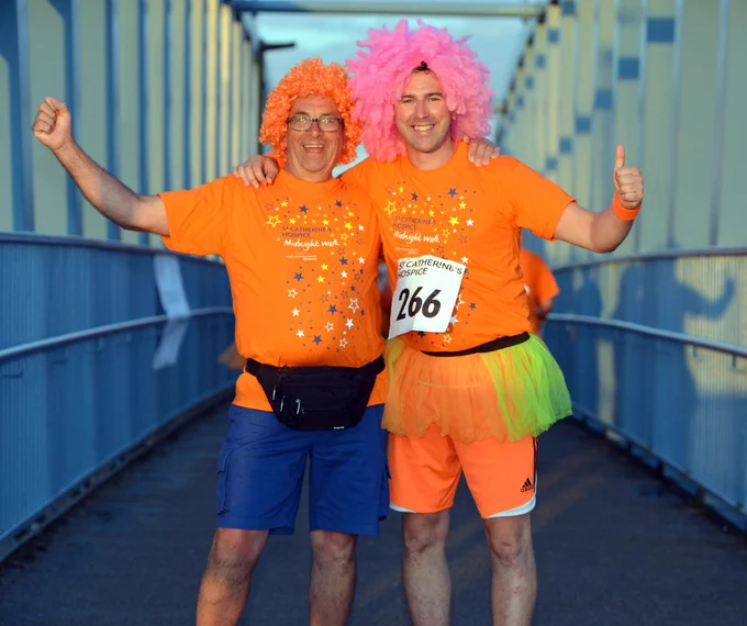 Two Midnight Walkers wearing orange t-shirts and neon wigs, smiling and giving a thumbs up to the camera. 