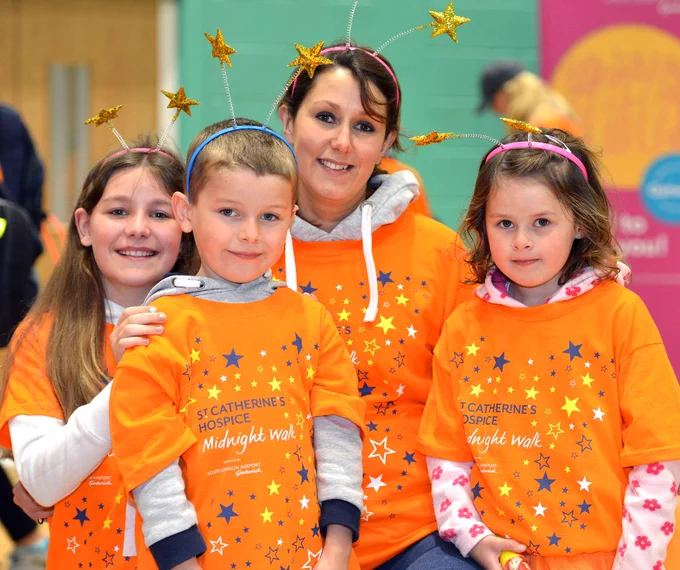 Four Midnight Walkers - one adult and three young children - all wearing orange Midnight Walk t-shirts and star head bands, smiling at the camera. 