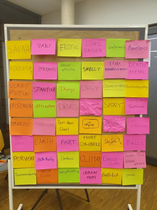 Several rows of colorful large Post Its with words on them on a pin wall.