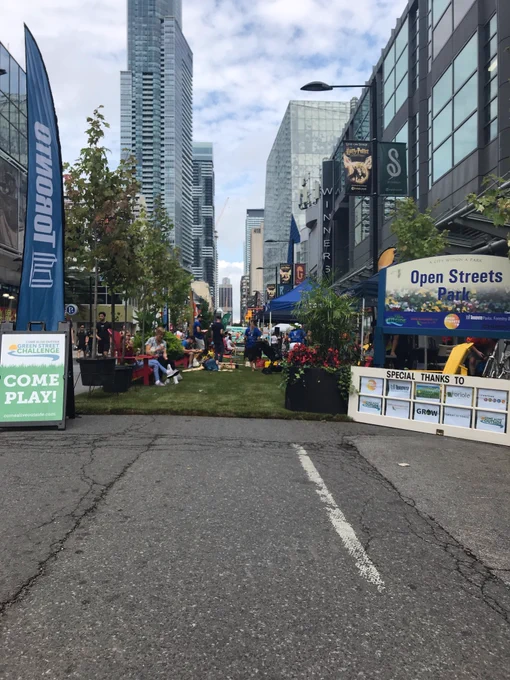 Sod grass covers the eastern lane of Yonge, now named Open Streets Park. Several children play on the grass with toys.