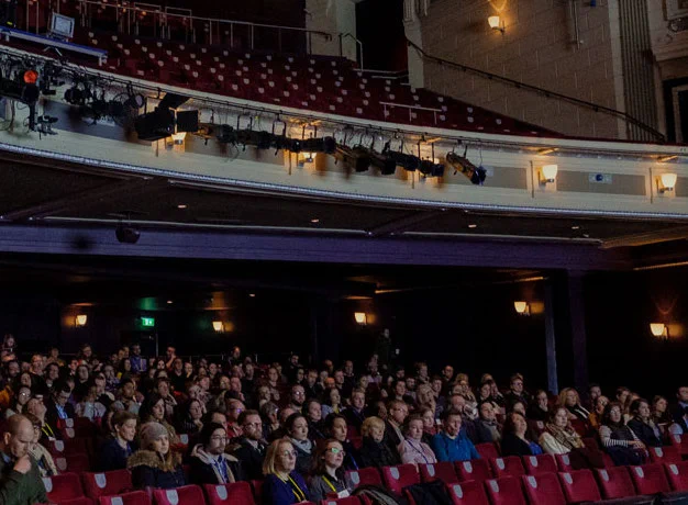 An audience sits in the red velvet seats in the Birmingham Hippodrome.

