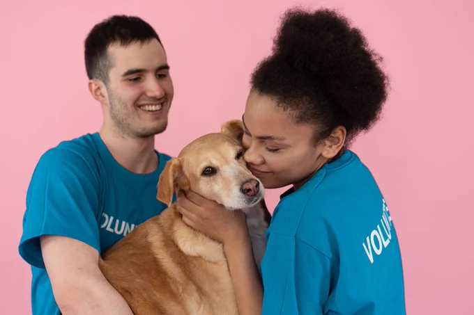 A man and woman in 'volunteer' t-shirts hugging a dog