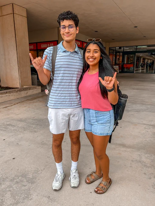 Two students doing the Roadrunner hand sign in front of the Student Union.