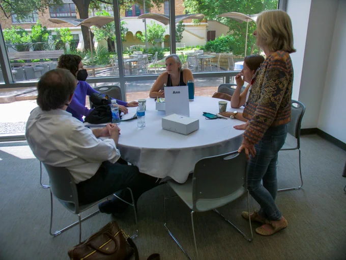 Group of four UT faculty sitting around a round table discussing a topic at NFS 22. Facilitator standing near the table listening. 