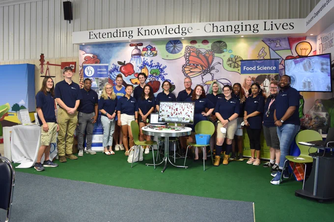 The group of Envision scholars stands in front of the Extension display at the Delaware State Fair.