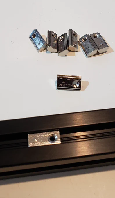 Ball spring t nut in black channel bar with a handful size pile of the same small Shiney metal components behind on a white background 