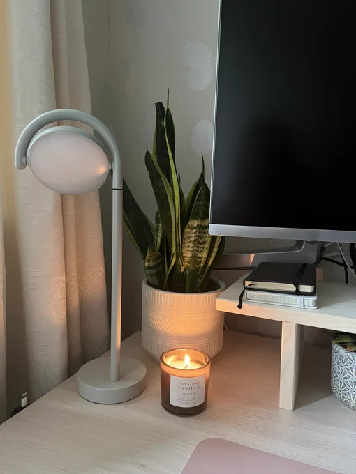 A dimly lit desk with a lit candle, plant and lamp