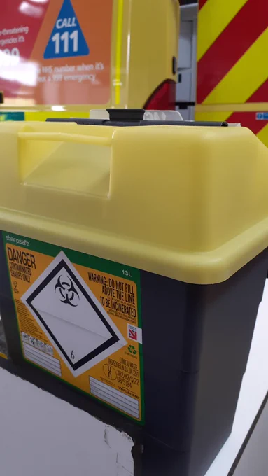 Sharps box with a yellow lid and a dark grey base