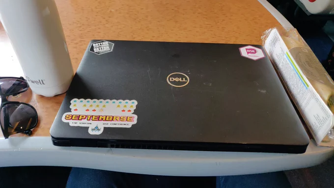 Scuffed black laptop on train table with a few stickers