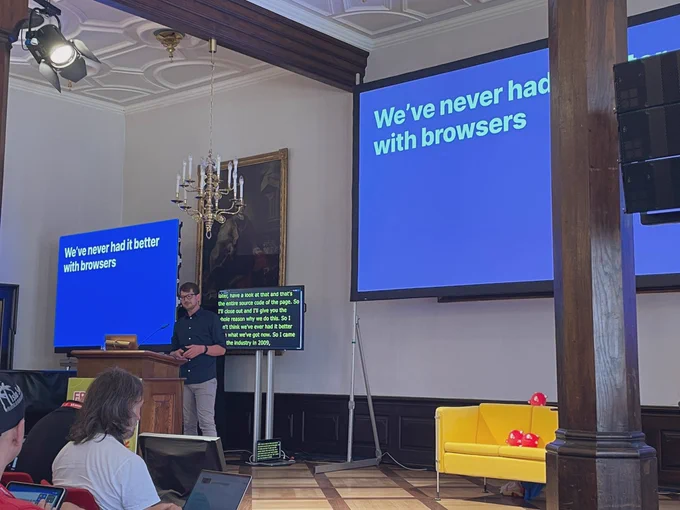 Andy Bell on stage with a slide in the background that says „We‘ve never had it better with browsers“