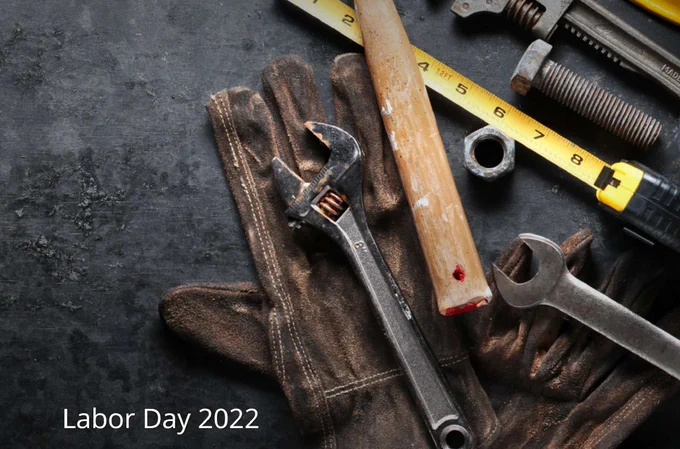 Close-up of tools, including a hammer, wrench, yellow tape measures, nuts & bolts, and a worker's glove. The background is dark, gritty.