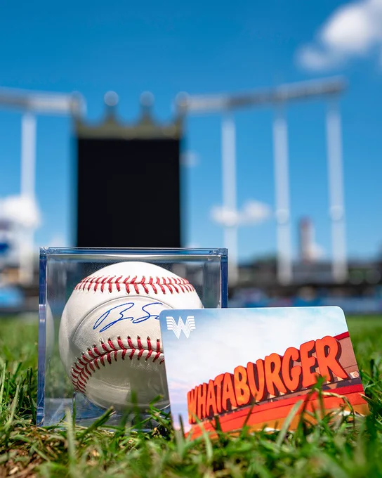 A photo of a baseball signed by Brady Singer next to a Whataburger gift card on the grass at Kauffman Stadium.