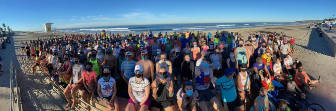 Hundreds of November Project members from around the world lined up shoulder to shoulder, wearing protective masks, posing for a panoramic post-workout group photo on the beach in San Diego.