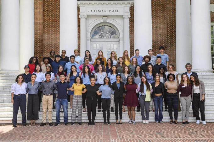 49 students comprising the 2022 Community Impact Internships Program cohort stand in four rows on the steps of Gilman Hall, smiling side by side for a photo.