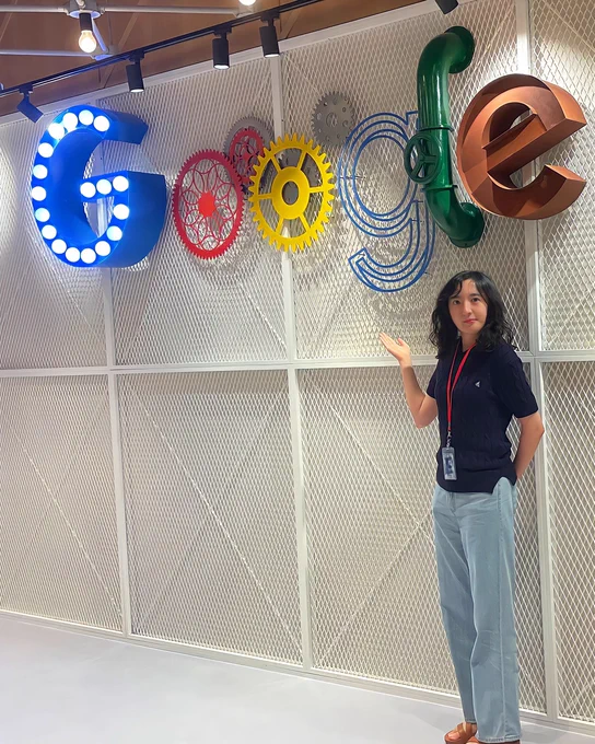 Sumin wearing a black shirt and blue jeans standing in front of a multi-color Google sign with a white gated background.