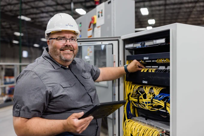 Jason holding a tablet and checking on a wire in an industrial panel.
